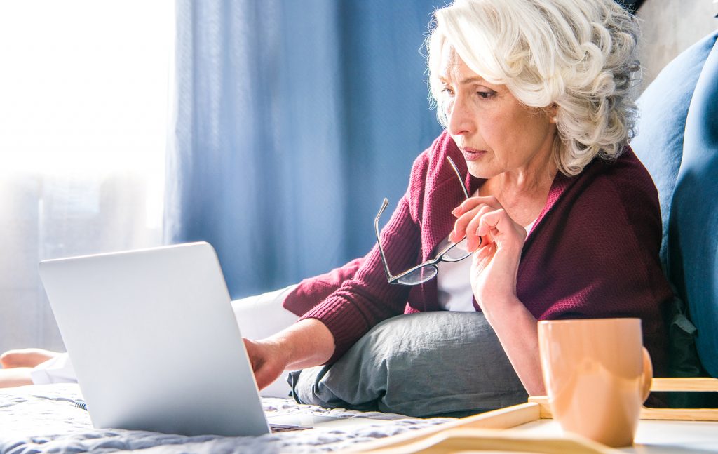 Senior woman sitting on a bed with a laptop, reading tips for Spider Solitaire