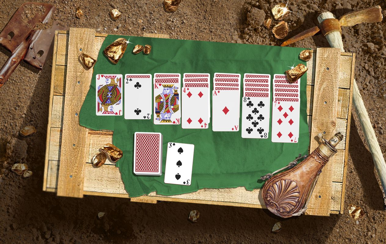 A Klondike Solitaire card layout on a wooden crate, set in a gold-rush scene with nuggets and mining gear.